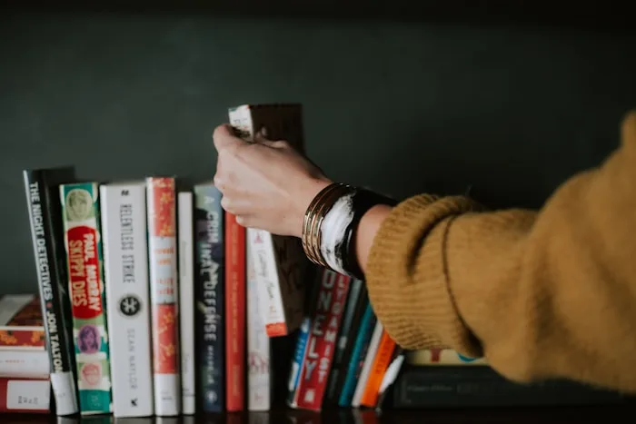 Bookshelf | CAQA Creative A hand reaches for a book on a shelf filled with titles, showcasing creative arts inspiration.