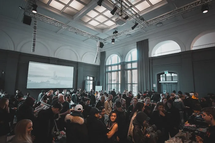 A large crowd enjoys a creative arts event in a bright, spacious hall with a projection screen.
