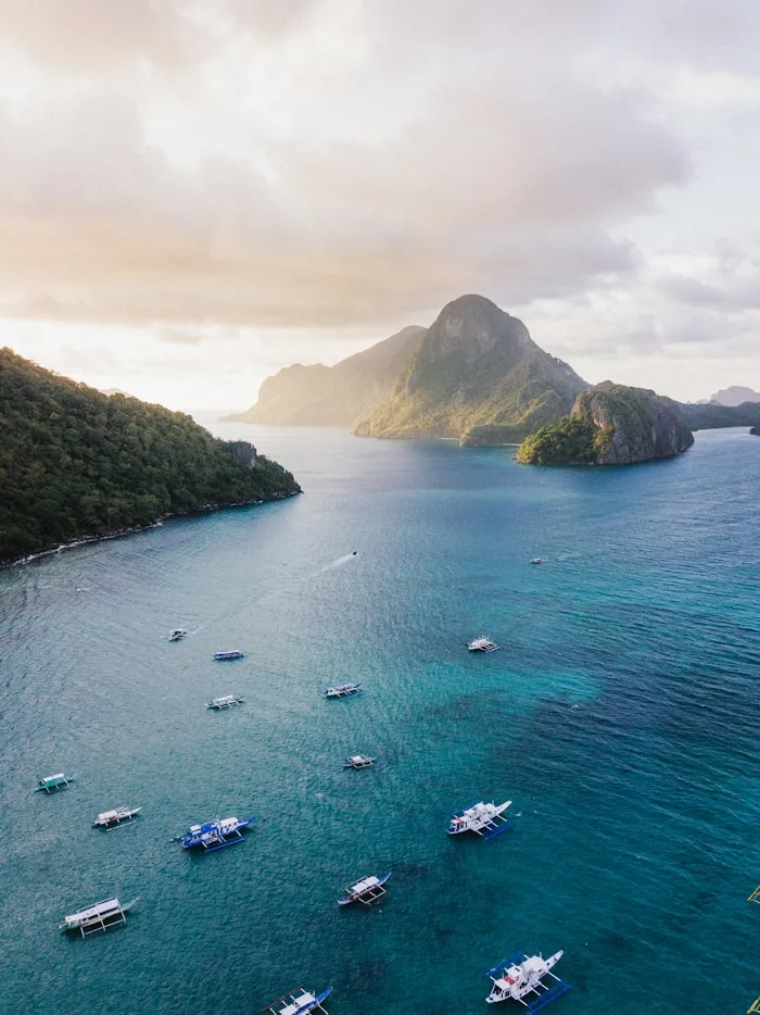 Boats float on turquoise waters near lush islands in El Nido, Palawan, showcasing beautiful tropical destinations.