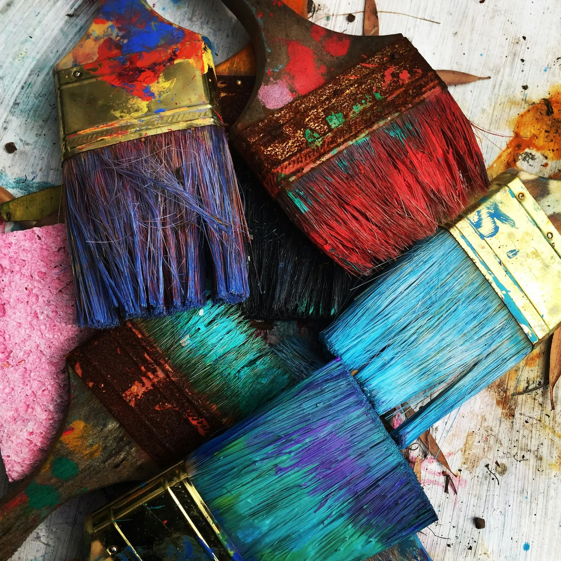 Used paintbrushes and a pink sponge rest on a colorful, splattered surface during creative arts training.